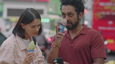 Genç bir çiftin dondurma yerken ve akıllı telefondan şehrin caddesinde dikilirken haritayı tartışırken orta boy fotoğrafı.