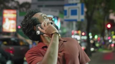 Göğüs hizasında cep telefonuyla konuşan ve geceleri caddede dikilirken etrafa bakan melez genç bir adam var.