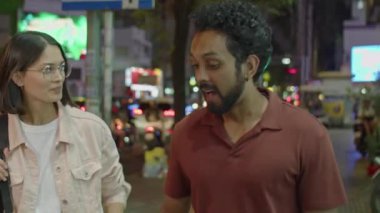 Genç, çok ırklı bir çiftin şehir caddesinde yürürken ve gece buluşurken tartıştıkları orta boy bir fotoğraf.