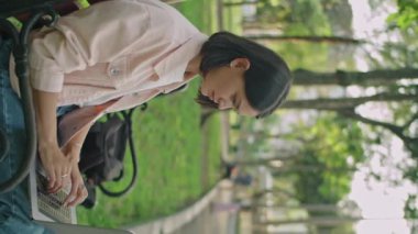 Genç esmer bir kadının parkta bankta oturup laptopla çalışırken düşünceli bakışlarını dikey çekimleri.