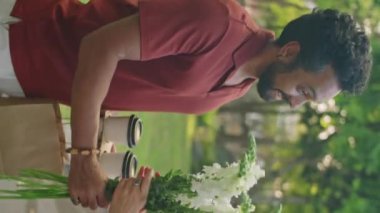 Erkek arkadaşın kadına çiçek buketi ve kahve fincanı verirken çekilmiş dikey bir fotoğrafı. Sonra da romantik bir buluşmada parkta onunla yürümüş.