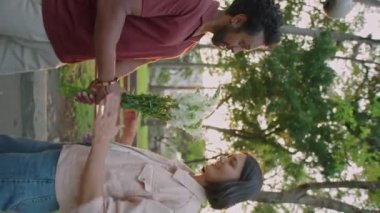 Dikey çekimde genç bir kadın bir buket çiçek alıyor, erkek arkadaşına teşekkür ediyor ve altın saat boyunca parkta romantik bir randevuda ona sarılıyor.