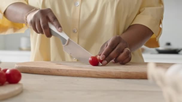 キッチンテーブルでチェリートマトを切ったアフリカ系アメリカ人女性の手を閉じ 自宅で夕食にサラダを準備する — ストック動画