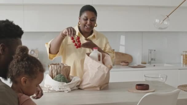 Afroamerikanische Mutter Lädt Lebensmittel Aus Einkaufstasche Auf Küchentisch Während Ihr — Stockvideo