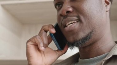 Afrika kökenli Amerikalı bir adamın evde cep telefonuyla konuşurken yakın plan çekimleri.