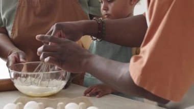 Afrika kökenli küçük tatlı bir kızın, anne babaya mutfakta birlikte yemek pişirirken malzemeleri karıştırmalarına yardım ettiği bir fotoğraf.