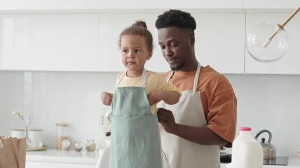 Młody Afroamerykanin Ojciec Pomaga Małej Córce Założyć Fartuch Przed Gotowaniem — Wideo stockowe