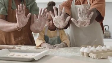 Afrika kökenli Amerikalı ailenin orta kesiminde kamerada un kaplı avuçlarını gösterirken küçük kızıyla mutfakta yemek pişirirken.