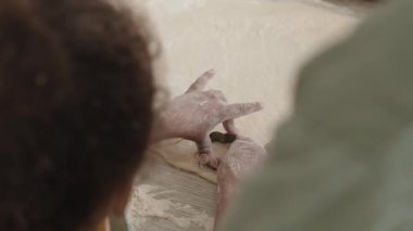 Mutfak masasından çiçek şeklindeki kurabiyeleri kesmek için metal kesiciler kullanan ebeveynlerin ve küçük çocukların omuzlarının üstünden aşağı doğru.