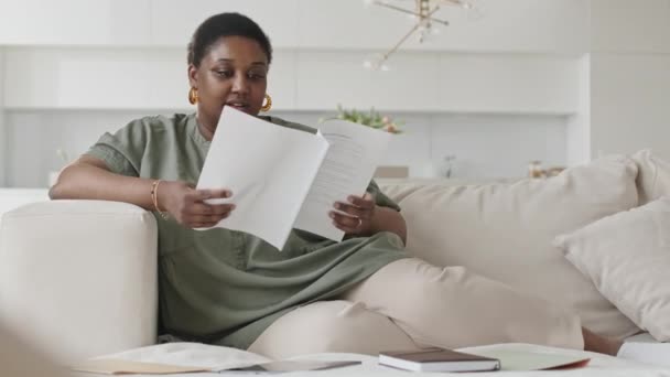 アフリカ系アメリカ人女性がリビングルームでソファーで休憩し 自宅で働いている間にビジネス用紙をチェック — ストック動画