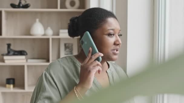 Średnie Ujęcie Afroamerykanki Stojącej Domu Patrzącej Przez Okno Rozmawiającej Przez — Wideo stockowe