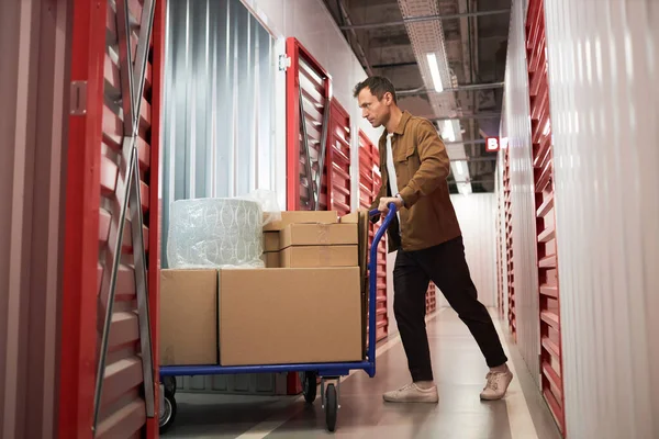 Man pushing cart with boxes inside unit he rents in self-storage facility