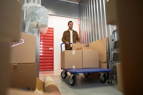 Customer pushing cart with belongings inside big unit he rented in self-storage