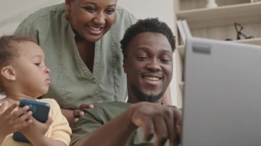 Mutlu Afrika kökenli Amerikalı askerin dizüstü bilgisayarda yazarken, gülümserken ve ekranda neşeli karısı ve küçük kızıyla tartışırken görüntüsünü kaldır.