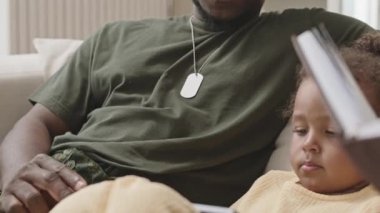 Afro-amerikalı şirin bir kızın dijital tabletle çizgi film seyrederken, ebeveynleri evde kanepede dinlenirken.