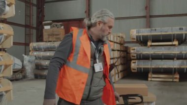 Büyük bir depoda iş günü kargo taşıyan bir depocunun orta boy fotoğrafı.