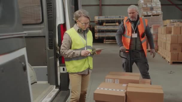 倉庫の貯蔵労働者とのバンへの貨物のローディングを制御するワークウェアの成熟した女性の中長いショット — ストック動画