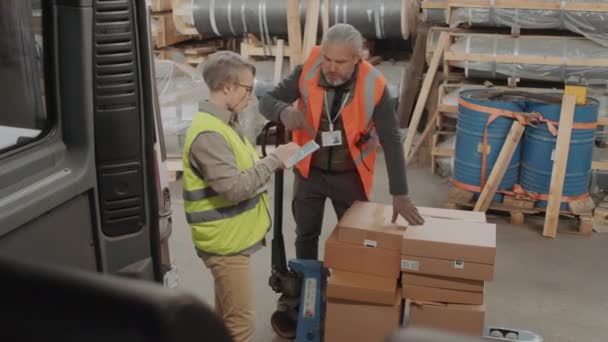 バンの隣に立って貨物輸送について男性労働者と話しながらデジタルタブレットを保持する女性倉庫の中長いショット — ストック動画