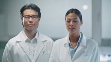 Laboratuvarda çalışırken beyaz önlüklü Asyalı erkek ve kadın bilim adamlarının birlikte poz verdikleri portre.