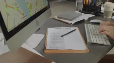 Depodaki iş belgeleriyle uğraşırken bilgisayardaki dağıtım haritasını kullanan tanınmayan kişinin görüntüsü.