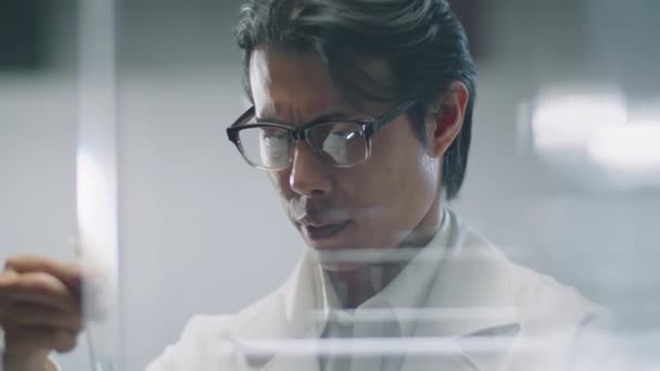 Vista Através Parede Vidro Cientista Asiático Macho Derramando Química Azul — Vídeo de Stock
