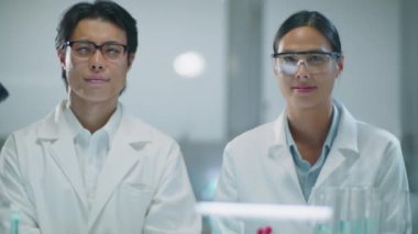 Beyaz önlüklü ve gözlüklü Asyalı erkek ve kadın kimyagerlerin portresi laboratuardaki iş yerinde kameraya poz veriyor.