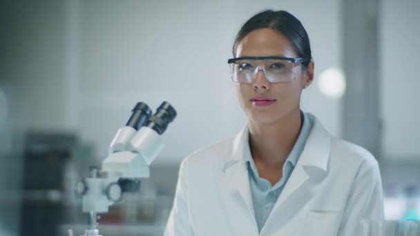 Laboratuvarda Mikroskopla Otururken Kameraya Poz Veren Koruyucu Gözlüklü Beyaz Ceketli — Stok video