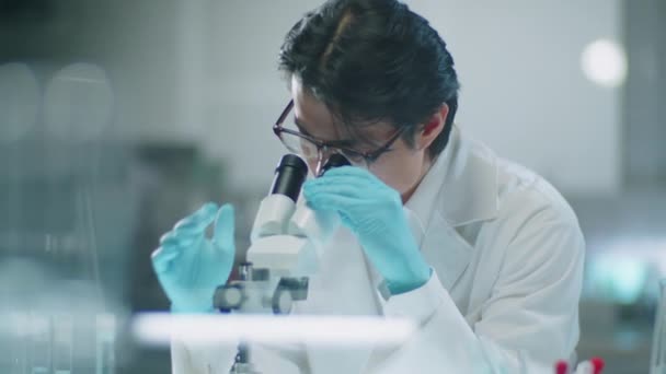 Мужчина Азиатский Ученый Лабораторном Халате Защитных Перчатках Просматривающий Микроскоп Записывающий — стоковое видео