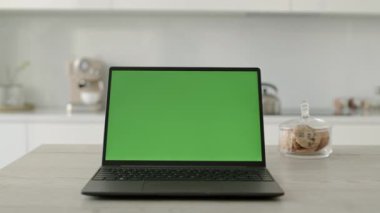Minimalist beyaz mutfaktaki masada yeşil renkli anahtar ekranlı dizüstü bilgisayardan çekilen kimse yok.