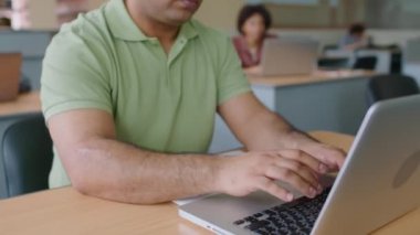 Modern kütüphanede çeşitli insanlarla çalışırken dizüstü bilgisayarda yazan Orta Doğulu genç göçmen öğrencileri yukarı kaldır.