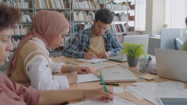 Modern kütüphanede masada oturan, uluslararası dil okulunda birlikte eğitim görürken İngilizce sınavı yazan genç göçmen öğrencilerin belini kaldırın.