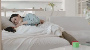 Küçük kızıyla birlikte Asyalı anne minimalist beyaz stüdyo dairelerinde yumuşak beyaz battaniyenin altında yatıp gündüz vakti birlikte uyuyorlar.