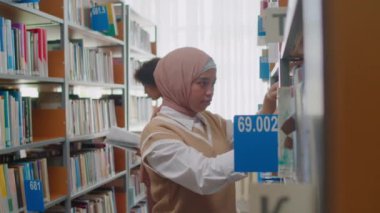 Üniversite kütüphanesinde kitap arayan tesettürlü Müslüman öğrenci yavaşlığı