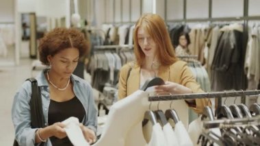 Modaya uygun tasarımcı dükkanında birlikte alışveriş yaparken şık giysilere bakan iki çekici, çok kültürlü kadının orta boy fotoğrafı.