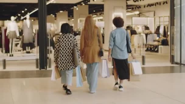 大きなモダンなショッピングモールでスタイリッシュな服店に入る3人の多民族の若い女性のフルバックビューショット — ストック動画