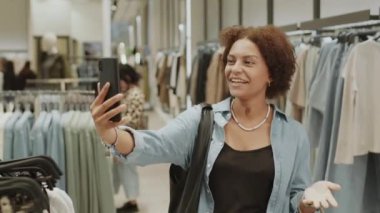 Çekici, Afro-Amerikalı genç bir kadının şık bir butikte kıyafet alışverişi yaparken arkadaşlarıyla telefonda sohbet ederken çekilmiş orta ölçekli bir fotoğrafı.