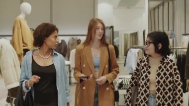 Üç farklı kız arkadaşın hafta sonları şık giyim mağazasında yürürken sohbet ederken, birlikte alışveriş yaparken orta boy bir fotoğraf.