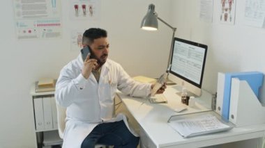 Ortadoğulu ciddi bir erkek doktorun hastaların göğüs röntgenlerini incelerken telefonla konuştuğu bir fotoğraf.