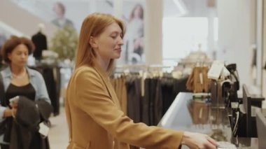 Modern tasarımcı galerisinden elbise alırken uzun düz kızıl saçlı, orta boy, çekici, beyaz bir kadın kredi kartı kullanıyor.