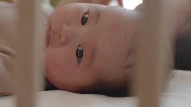 Gündüzleri kız kardeşiyle yumuşak beşiğinde uzanan sevimli Asyalı bir çocuğun ahşap beşik raylarından