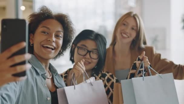 在当代大商场里 三个快乐而又多姿多彩的女友拿着购物袋在智能手机上自拍 — 图库视频影像