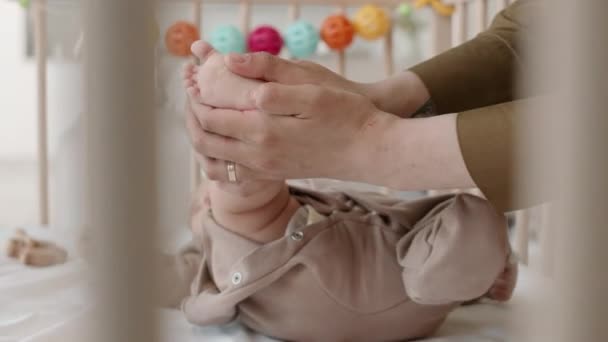在舒适的家 当他躺在柔软的婴儿床里时 一个无法辨认的女人轻柔地按摩着小宝宝的脚趾头和脚后跟 — 图库视频影像