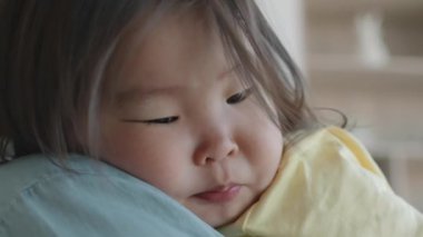 Kapalı otururken annesinin omzuna yaslanan uykulu Asyalı küçük kızın yakın çekimi.