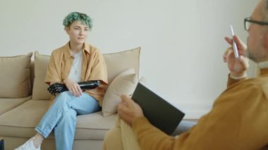 Kolu protez ve mavi saçlı bir kızın omzunun üstünden. Koltukta oturup, danışmanlık sırasında psikologla konuşuyor.