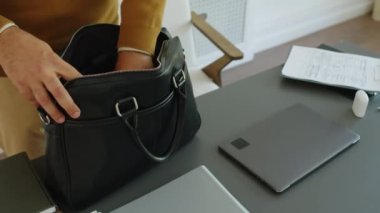 Erkek terapistin deri evrak çantasından aletlerini çıkardığı, masa başında oturduğu ve işe başlarken dizüstü bilgisayar kullandığı yüksek açılı bir fotoğraf.