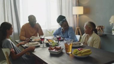 Afrika kökenli Amerikalı anne, baba ve iki kız Kwanzaa 'da yemek yemeden önce yemek masasında el ele tutuşup, gözleri kapalı dua ediyorlar.