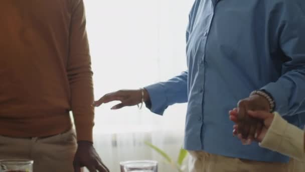 夕食テーブルの周りに立っているアフリカ系アメリカ人の家族のクロップショット 自宅でお祝いの夕食の前に手を握り — ストック動画