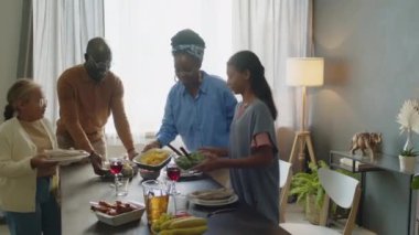 Mutlu Afrika kökenli Amerikalı ebeveynler ve iki kız evde aile kutlaması için hazırlanırken yemek masasında servis ediyorlar.