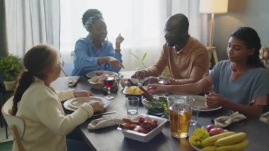 Afro-Amerikan anne, baba ve iki kız yemek masasında oturup, konuşuyorlar ve tatillerini evde kutluyorlar.