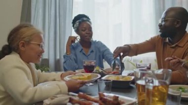 Afro-Amerikalı ebeveynler ve iki kız evde tatil yemeği yerken yemek, gülümsemek ve sohbet etmek.